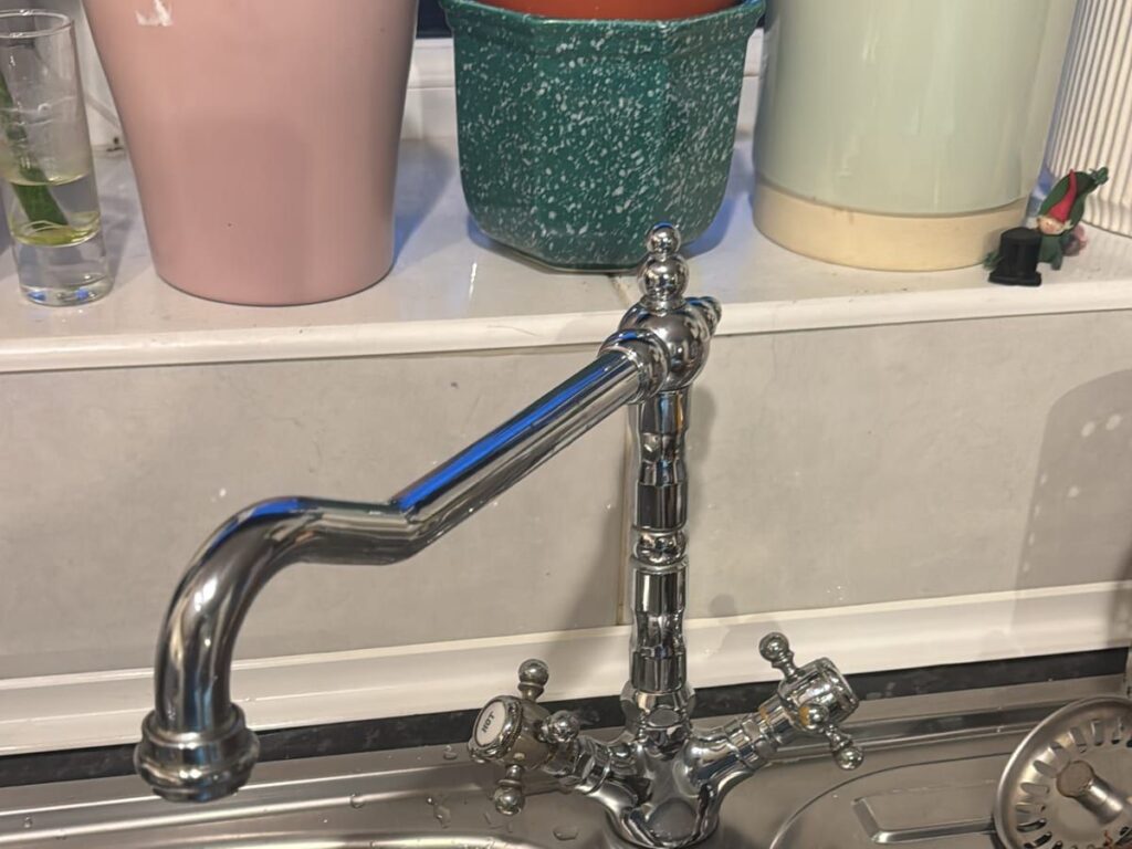 Traditional chrome bridge mixer tap installed over a stainless steel kitchen sink.