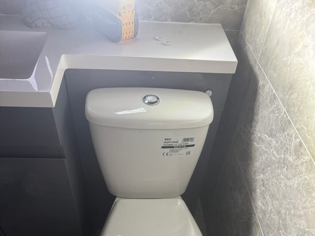 Newly installed white close-coupled toilet against a tiled bathroom wall.