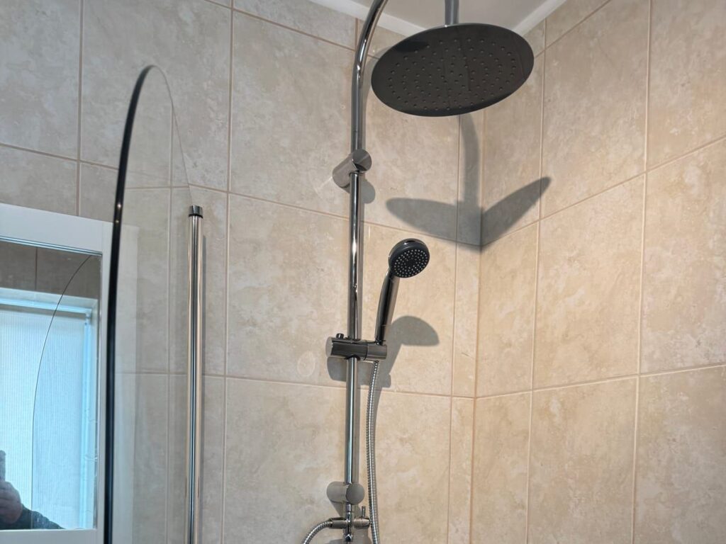 Shower riser rail with a black rainfall head and hand shower in a tiled shower enclosure.