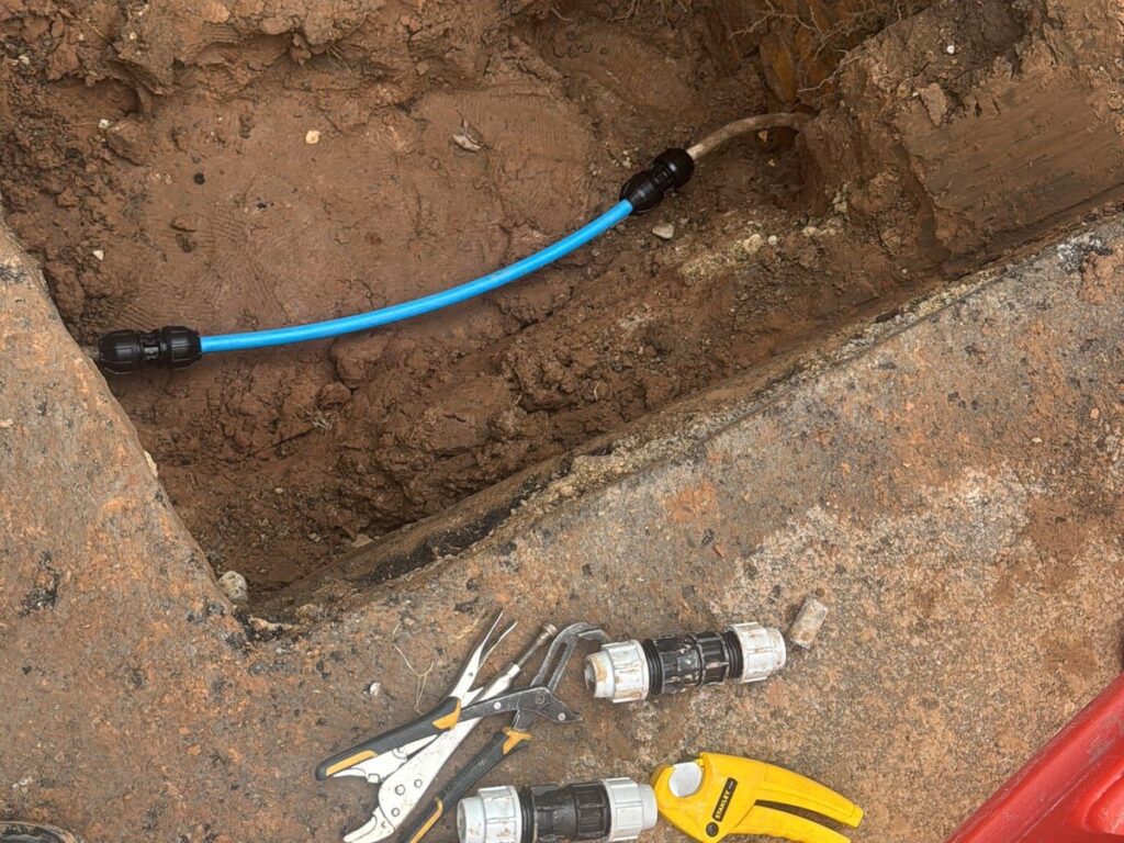 Blue MDPE water main laid in an open trench and joined with black compression fittings.