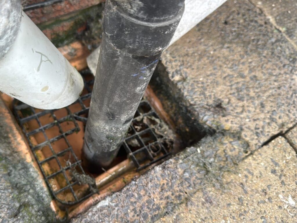 Drain rod inserted into an external gully alongside a downpipe.